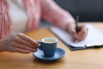 Coffee break. Woman with cup writing at wooden table indoors, closeup