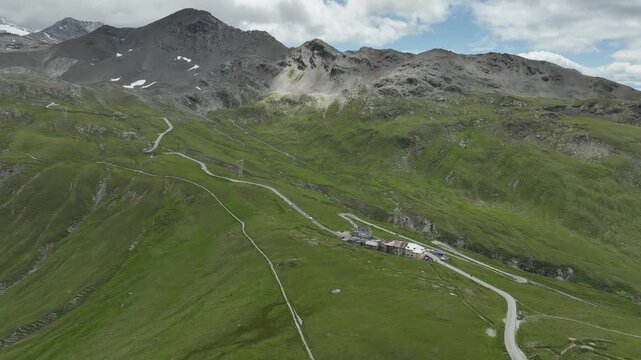 Aerial view of winding roads cutting through lush green mountain slopes, contrasted against the rugged, rocky terrain of Passo dello Stelvio, Stilfs, Lombardia, Italy.
