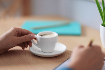 Coffee break. Woman writing with cup at wooden table indoors, closeup