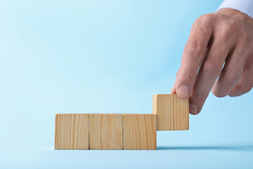 Man with wooden cubes on light blue background, closeup. Space for text
