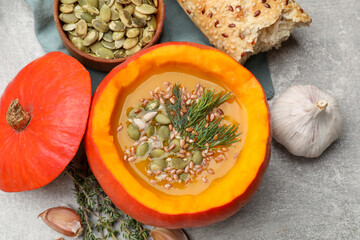 Tasty pumpkin cream soup with seeds, herbs, garlic and bread on grey textured table, flat lay