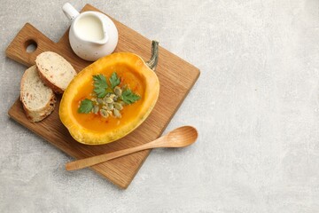 Tasty pumpkin cream soup with seeds, parsley and bread on grey textured table, top view. Space for text