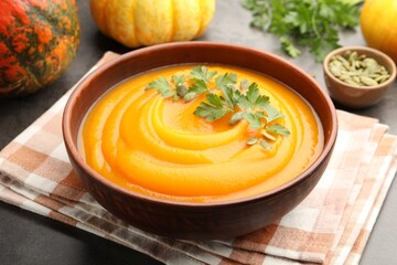 Tasty pumpkin cream soup with parsley and seeds in bowl on gray table, closeup