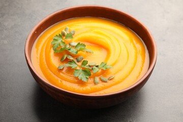 Tasty pumpkin cream soup with parsley and seeds in bowl on gray textured table, closeup