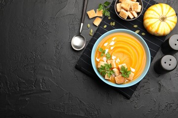 Tasty pumpkin cream soup with parsley and croutons served on dark textured table, flat lay. Space for text