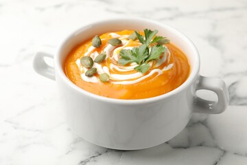 Tasty pumpkin cream soup with parsley and seeds in bowl on white marble table, closeup