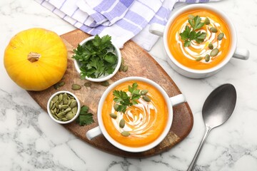Tasty pumpkin cream soup with parsley and seeds served on white marble table, flat lay