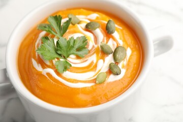 Tasty pumpkin cream soup with parsley and seeds in bowl on light table, closeup