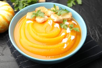 Tasty pumpkin cream soup with parsley and croutons in bowl on dark table, closeup