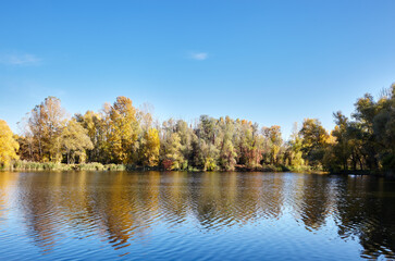 Beautiful river landscape at Autumn. The surface of the water against the background of trees and a blue sky on a sunny perfect day. The bright colors of fall