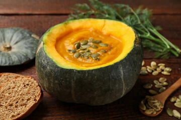 Tasty pumpkin cream soup with seeds and thyme served in pumpkin on wooden table, closeup
