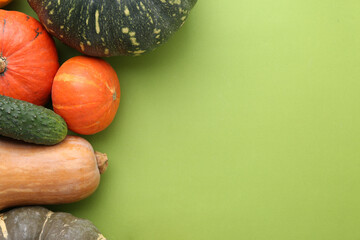 Many fresh pumpkins and cucumber on green background, flat lay with space for text. Gourd vegetables