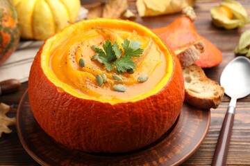 Tasty pumpkin cream soup with seeds and parsley served in pumpkin on wooden table, closeup