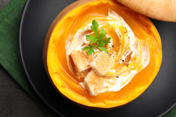 Tasty pumpkin cream soup with croutons and parsley served in pumpkin on grey table, top view