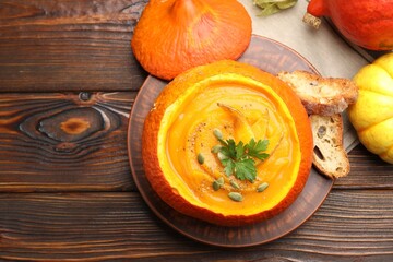 Tasty pumpkin cream soup with seeds and parsley served in pumpkin on wooden table, flat lay. Space for text