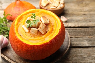Tasty pumpkin cream soup with croutons and parsley served in pumpkin on wooden table, closeup