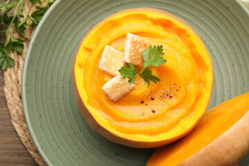 Tasty pumpkin cream soup with parsley and croutons served in pumpkin on wooden table, top view