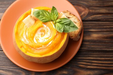 Tasty pumpkin cream soup with basil and croutons served in pumpkin on wooden table, top view