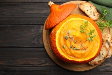 Tasty pumpkin cream soup with parsley and seeds served in pumpkin on wooden table, top view. Space for text