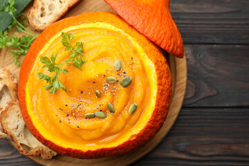 Tasty pumpkin cream soup with parsley and seeds served in pumpkin on wooden table, top view