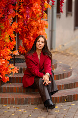 Portrait of a young woman with leaves in an autumn park. A stylish girl in a burgundy jacket strolls outdoors. Autumn fashion.