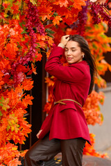 Portrait of a young woman with leaves in an autumn park. A stylish girl in a burgundy jacket strolls outdoors. Autumn fashion.