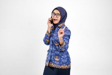 Cheerful Indonesian civil servant woman in blue batik uniform talking on smartphone while smiling...