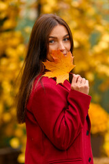 Portrait of a young woman with leaves in an autumn park. A stylish girl in a burgundy jacket strolls outdoors. Autumn fashion.