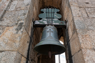 Naklejka premium Sino de bronze antigo com uma cruz a meio, suspenso numa estrutura de madeira envelhecida entre paredes de cantaria rústica numa torre de uma Igreja