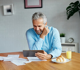 Senior man checking bills and calculating expenses using a tablet computer at home, debt taxes and...