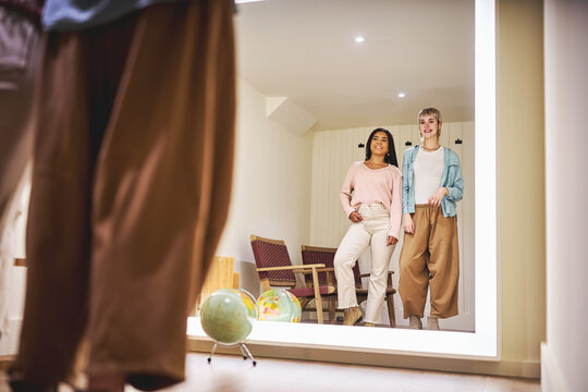 Two women looking at their reflection while trying on clothes - Powered by Adobe