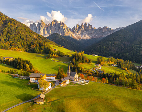 Aerial view of the iconic church nestled amidst rolling hills and golden-hued trees, set against the dramatic backdrop of the Dolomites, St. Magdalena, Trentino-South Tyrol, Italy.