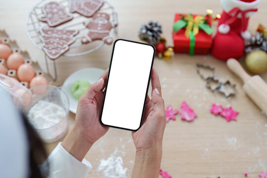 Holiday Recipe Search. A woman holding a smartphone while preparing for Christmas baking.