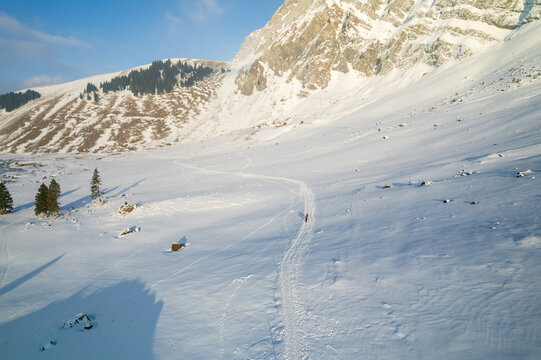 Aerial view of a snow-covered valley floor leading towards the towering, rocky peaks under a clear sky, Switzerland.
