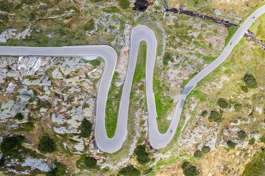 Aerial view of a winding road cutting through the rugged, rocky landscape, contrasting with patches of vibrant green, Grimsel Pass, Switzerland.
