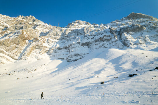 Aerial view of snow-capped peaks and a lone figure traversing the pristine white expanse of the Swiss Alps under a vibrant blue sky, Engelberg, Switzerland.