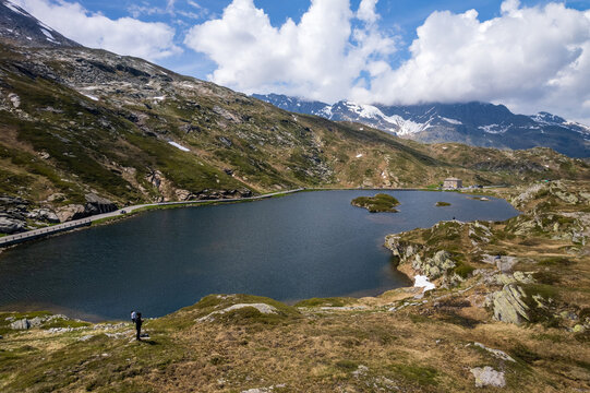 Aerial view of the shimmering dark lake reflecting the surrounding rugged mountains under a sky dotted with fluffy white clouds, Simplon Pass, Switzerland.