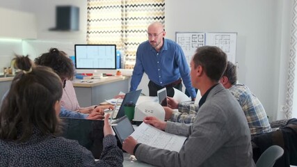 Corporate meeting in a modern office where bald team leader scolds employees for mistakes. Tense atmosphere as workers sit silently, manager expresses critique. Blueprints and laptops on the table. - Powered by Adobe