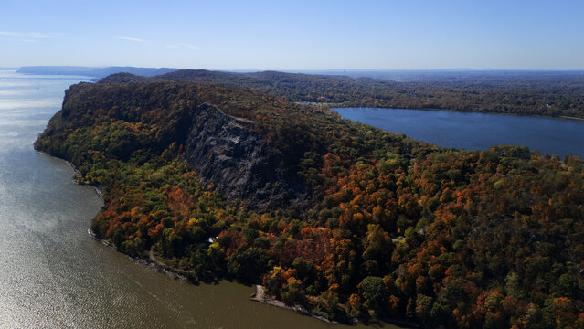 Aerial view of autumn foliage ablaze with fiery hues clinging to the rocky cliffs overlooking the tranquil water, N Rte 9W, Nyack, New York, United States.