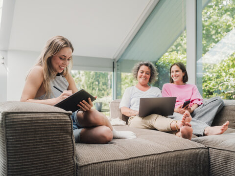 Mother and daughters cuddling on couch planning with laptop and tablet