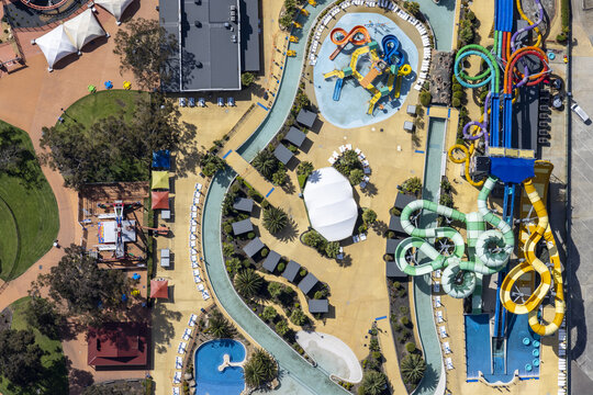 Aerial view of a vibrant water park with colorful slides twisting and turning amidst a landscape of pools and sun-drenched pathways, Tynong North, Victoria, Australia.