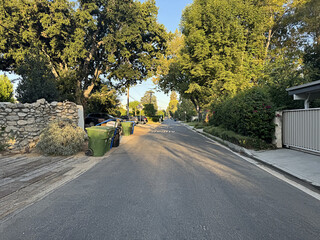 empty road in an American residential suburban neighborhood - houses, driveways, parked cars, trees and shrubs, trash cans bins, walls, homes - Los Angeles, California