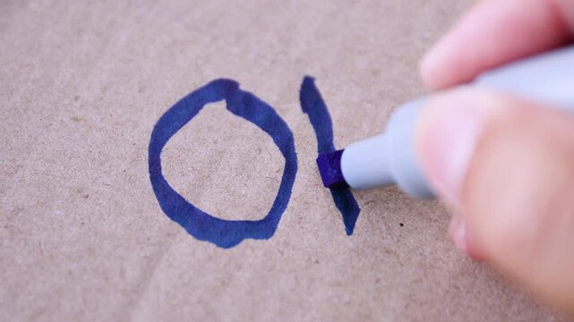 Hand writing "OK" with blue marker on cardboard, symbolizing approval, correctness, or a simple positive message, close-up