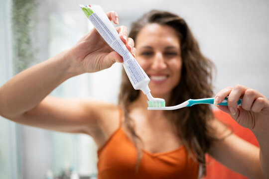Woman applying toothpaste to toothbrush in bathroom during morning routine