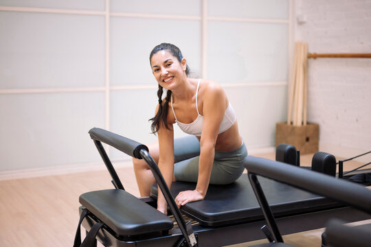Smiling pilates instructor sitting on reformer in gym after workout