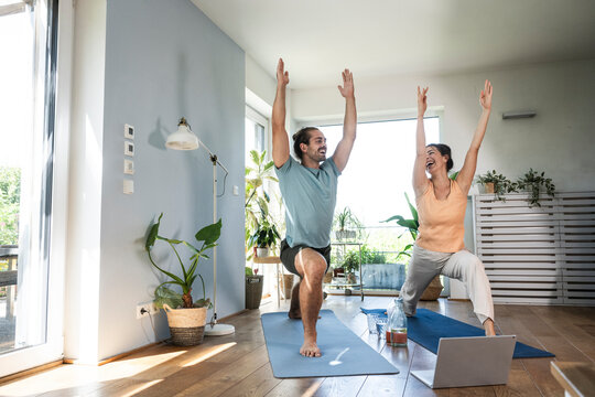 Happy couple doing stretching exercise near laptop at home