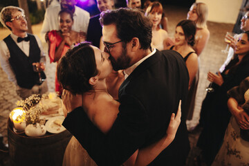 Wedding couple sharing a kiss among friends during a festive celebration