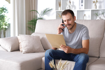 Man reading document and consulting on phone at home