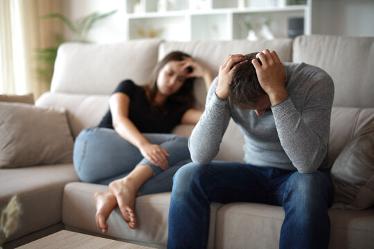 Desperate man suffering beside his sad wife at home