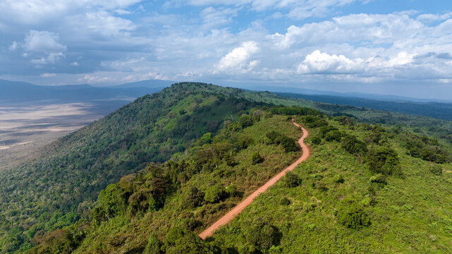 Aerial view of a winding dirt path cutting through the lush green hills overlooking Lake Magadi and the Ngorongoro Crater, Ngorongoro Crater, Arusha Region, Tanzania.